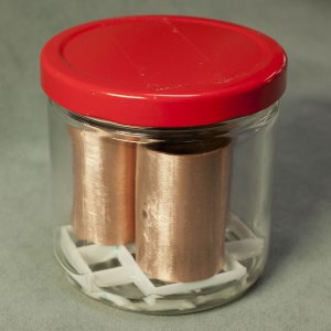Copper tube sections sitting on egg crate in glass jar with a small amount of vinegar at the bottom.